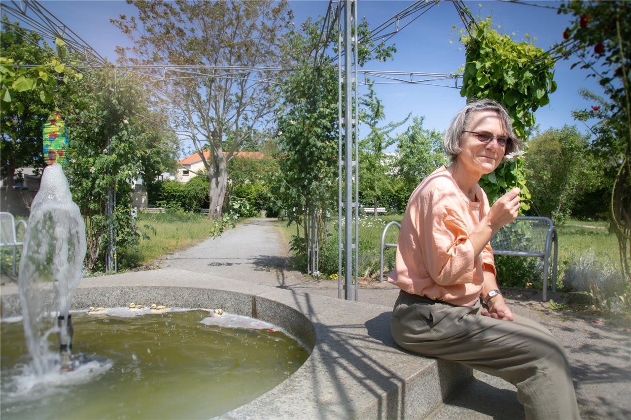 Brunnen im Park, auf dessen Rand eine ältere Dame sitzt